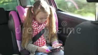 小女孩在车里用智能手机。 可爱的少女在智能手机上玩，而骑在后座上开车